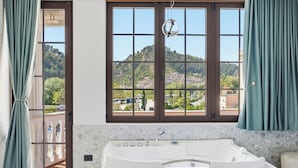 Une salle de bain avec une grande baignoire, une fenêtre donnant sur une colline et une porte dotée d’un panneau en verre.
