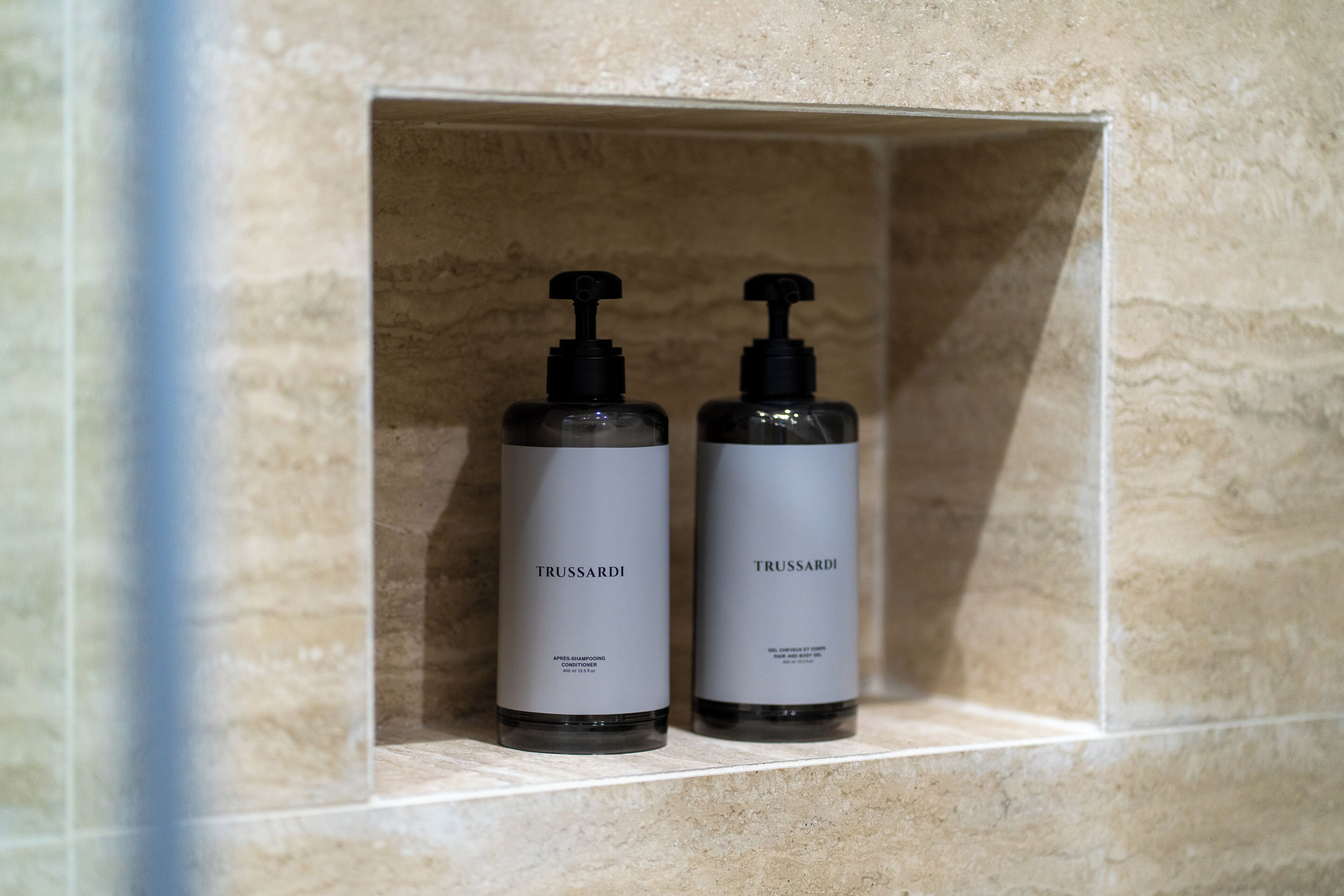 Dos ampolles de productes de cura de la pell Trussardi en un nínxol amb rajoles.
