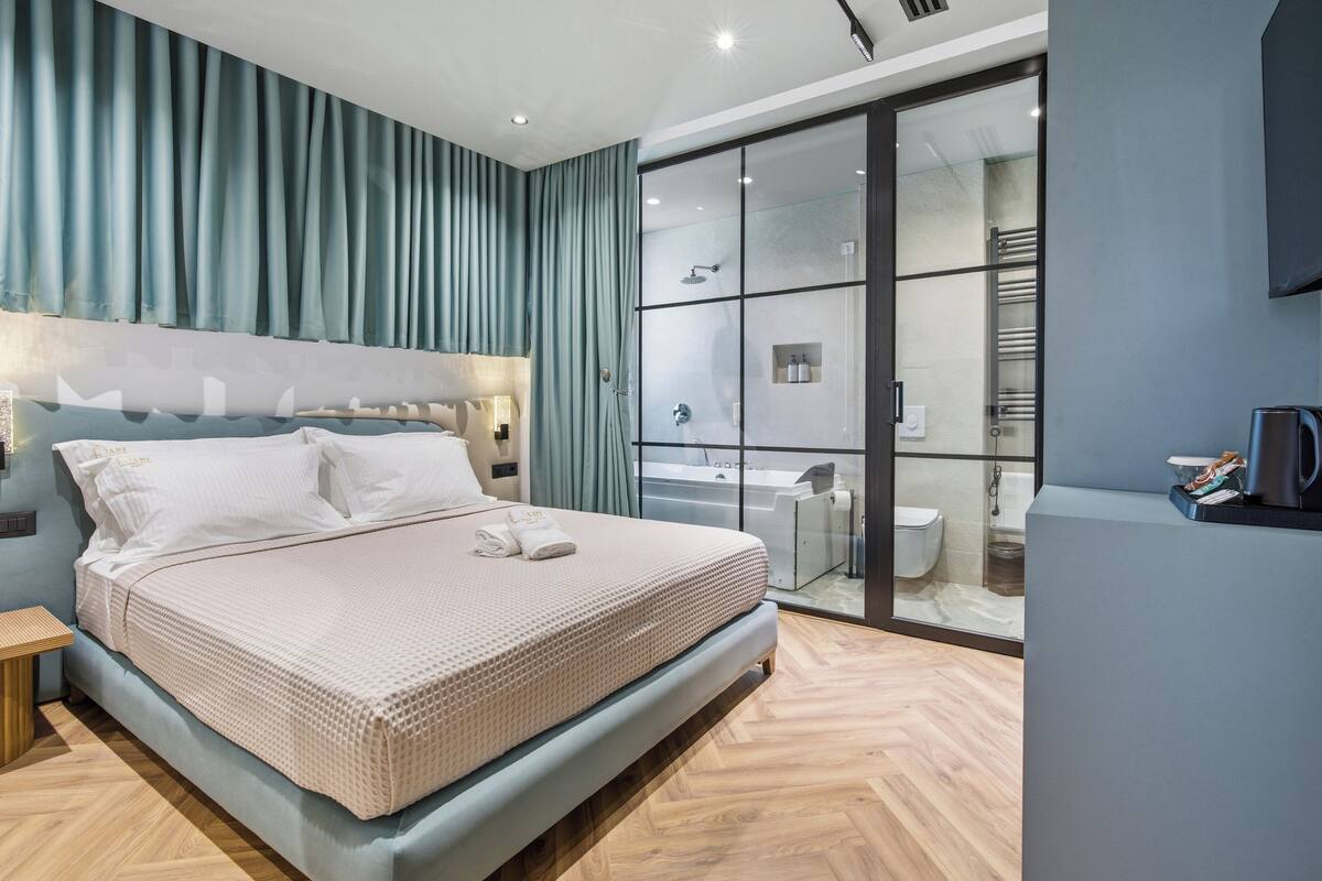 Quarto moderno com cama grande, box de vidro para o chuveiro e banheiro visível.