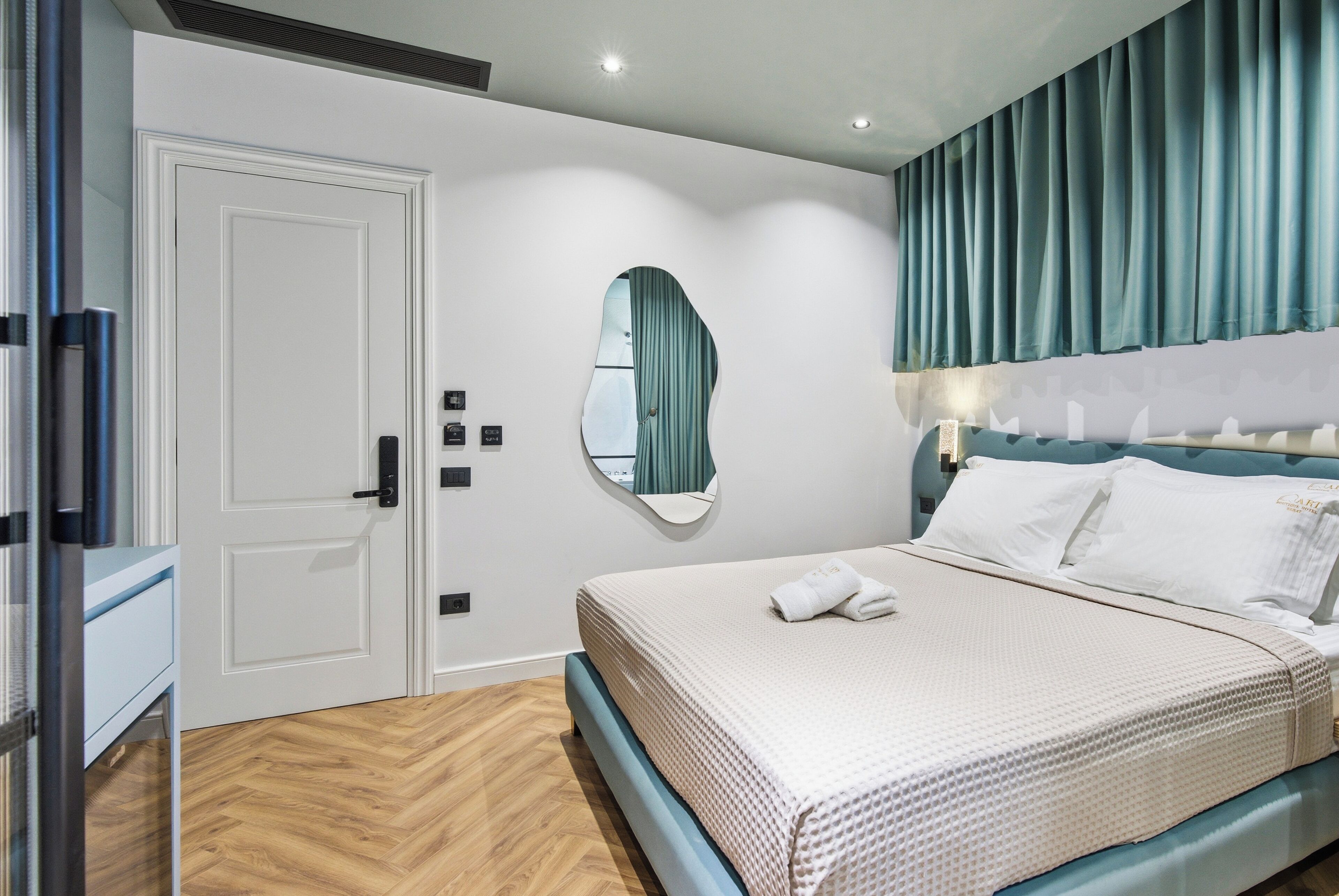 A bedroom with a bed, a door, a mirror, and a window with curtains.
