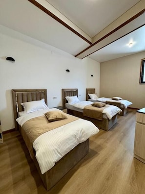 Habitación de hotel con tres camas, cabeceros de madera y suelo de madera.