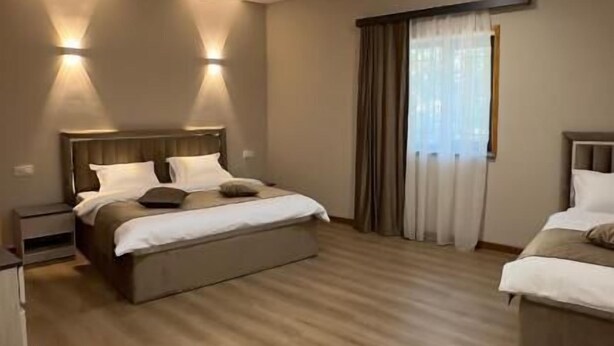 A hotel room with a large bed, bedside tables, a wardrobe, and a window with curtains. - MARCO Hotel (Goris)