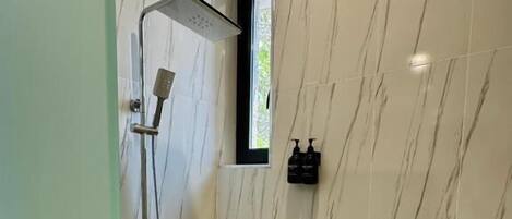A bathroom with a shower, marble walls, and a window.