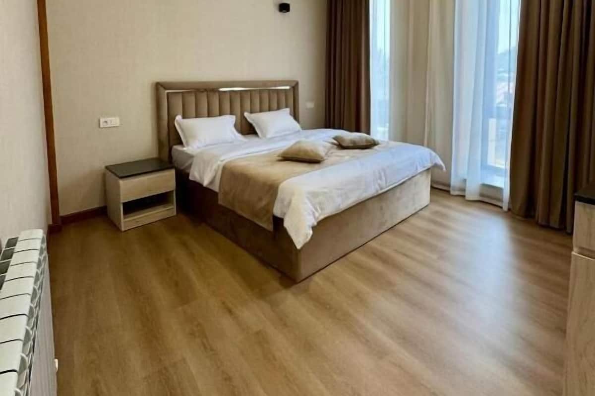 Una camera da letto con un letto, comodini, abat-jour e una finestra con tende.