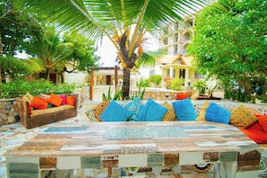 Un patio con un banco de mosaicos, un sofá de madera con cojines de colores y una palmera.