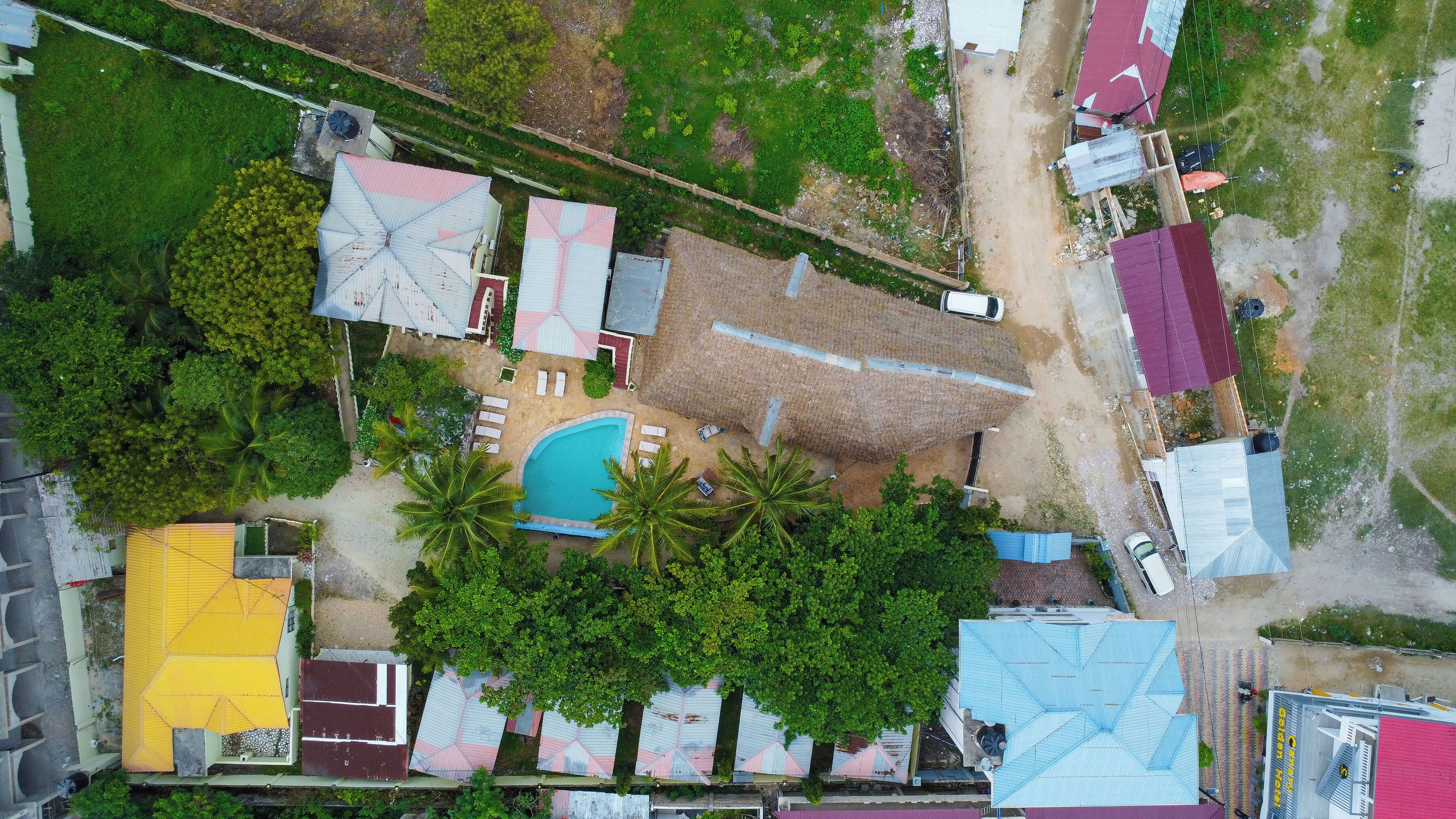 An aerial view of a residential area with a swimming pool, multiple houses, and a road.