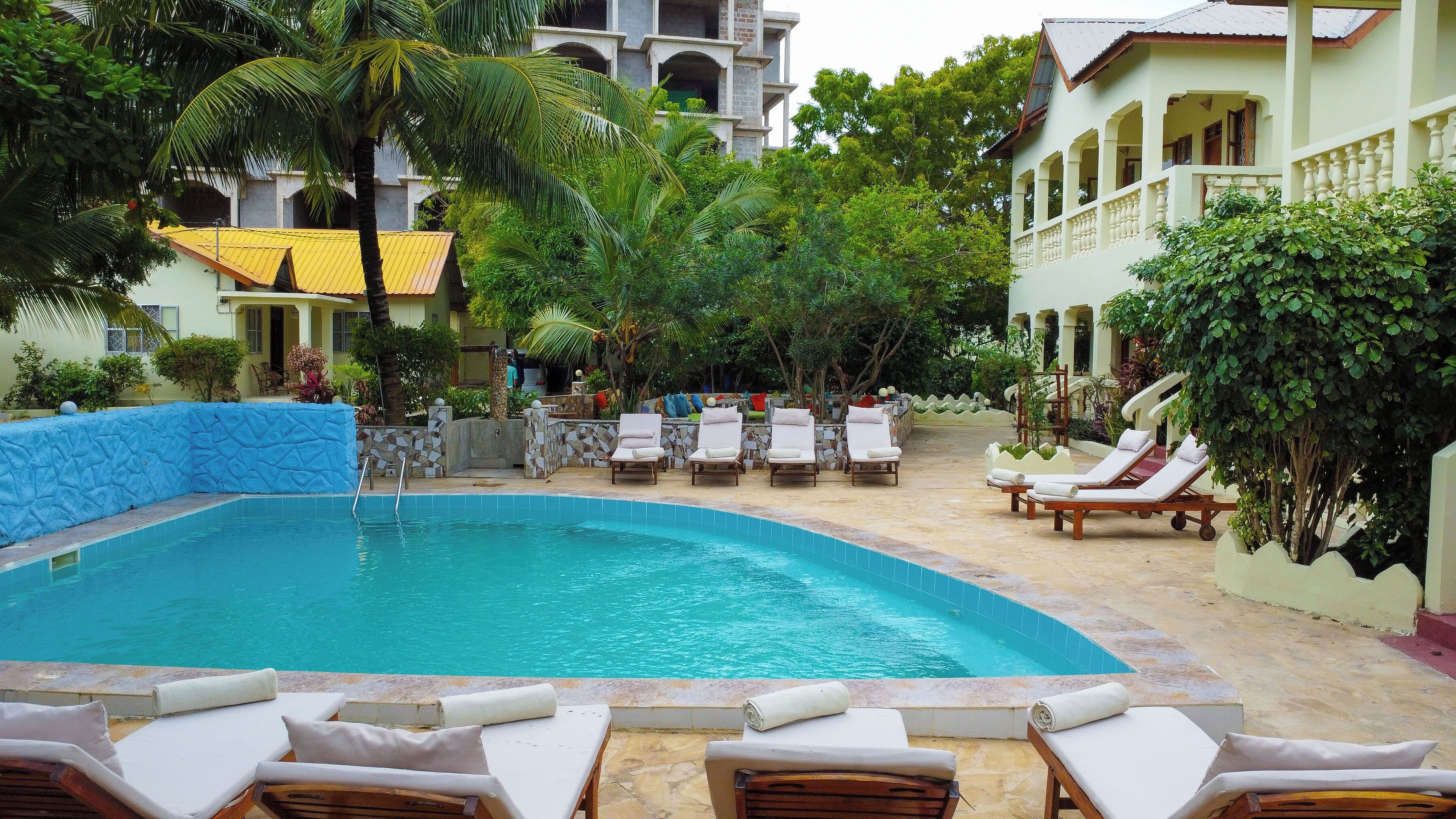 A swimming pool with lounge chairs, surrounded by greenery and a building with a tiled roof.
