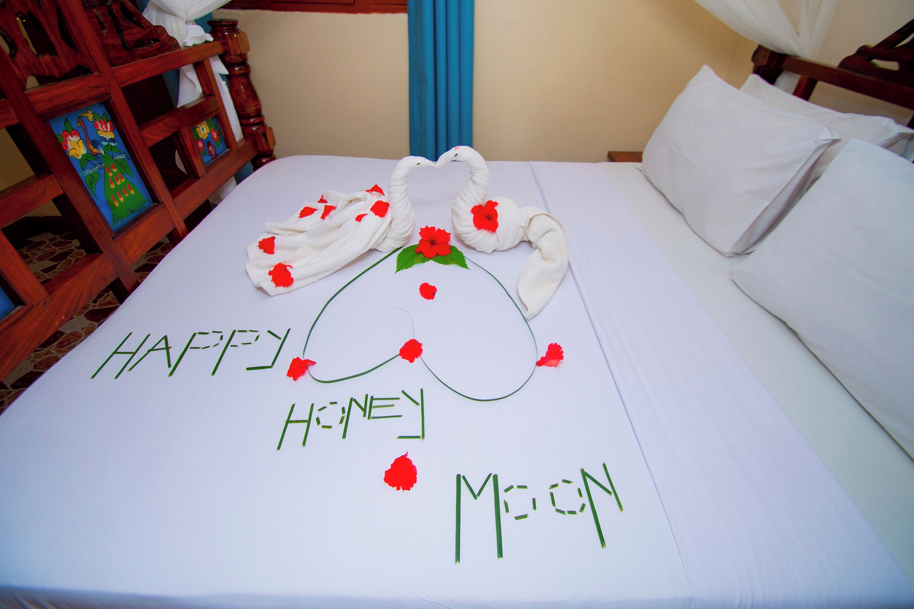 Una cama con un arreglo de toallas decorativo que deletrea 'HAPPY HONEY MOON' y una silla de madera con una pintura colorida.