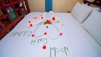 Una cama con un arreglo de toallas decorativo que deletrea 'HAPPY HONEY MOON' y una silla de madera con una pintura colorida.