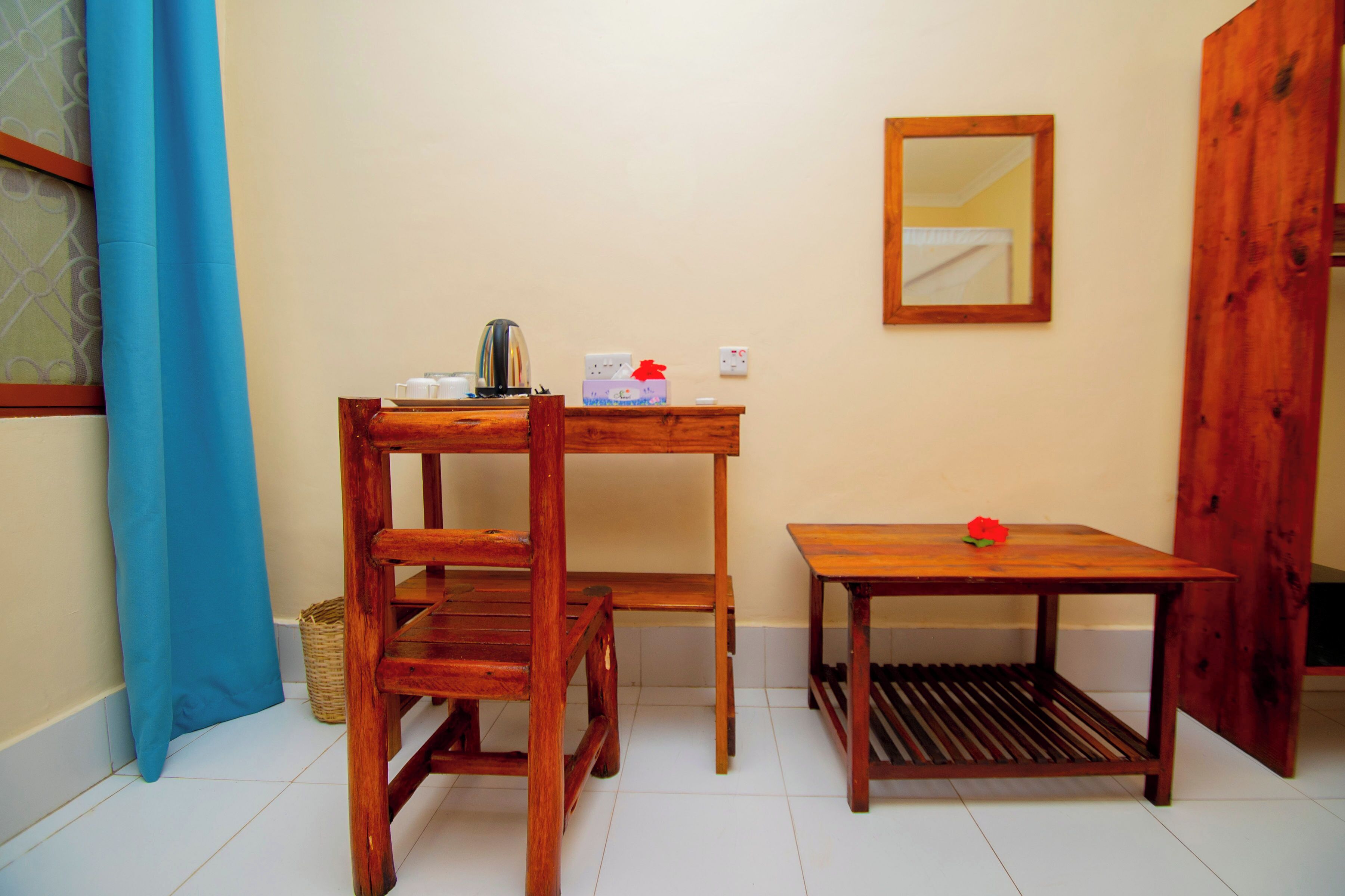 Une petite pièce avec un bureau en bois, une chaise, une petite table, un miroir et un rideau bleu.