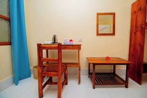 A small room with a wooden desk, a chair, a small table, a mirror, and a blue curtain. - Samridhi Bustani Oasis (Nungwi)