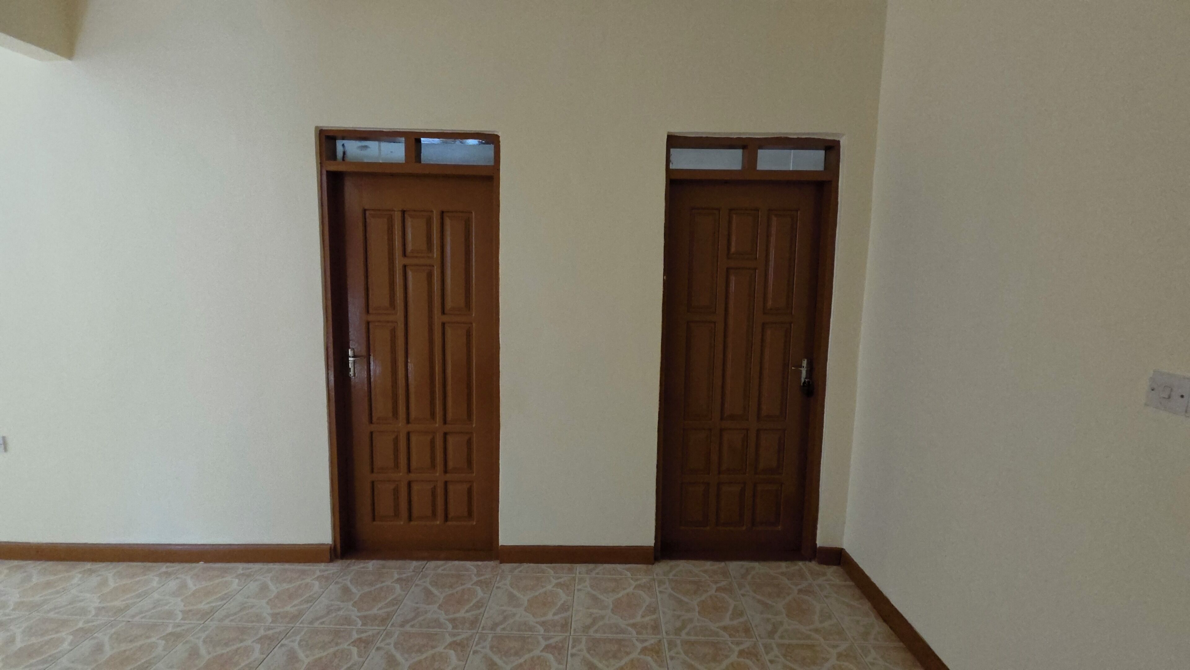 Una habitación con dos puertas de madera, piso de baldosas y una pared lisa.