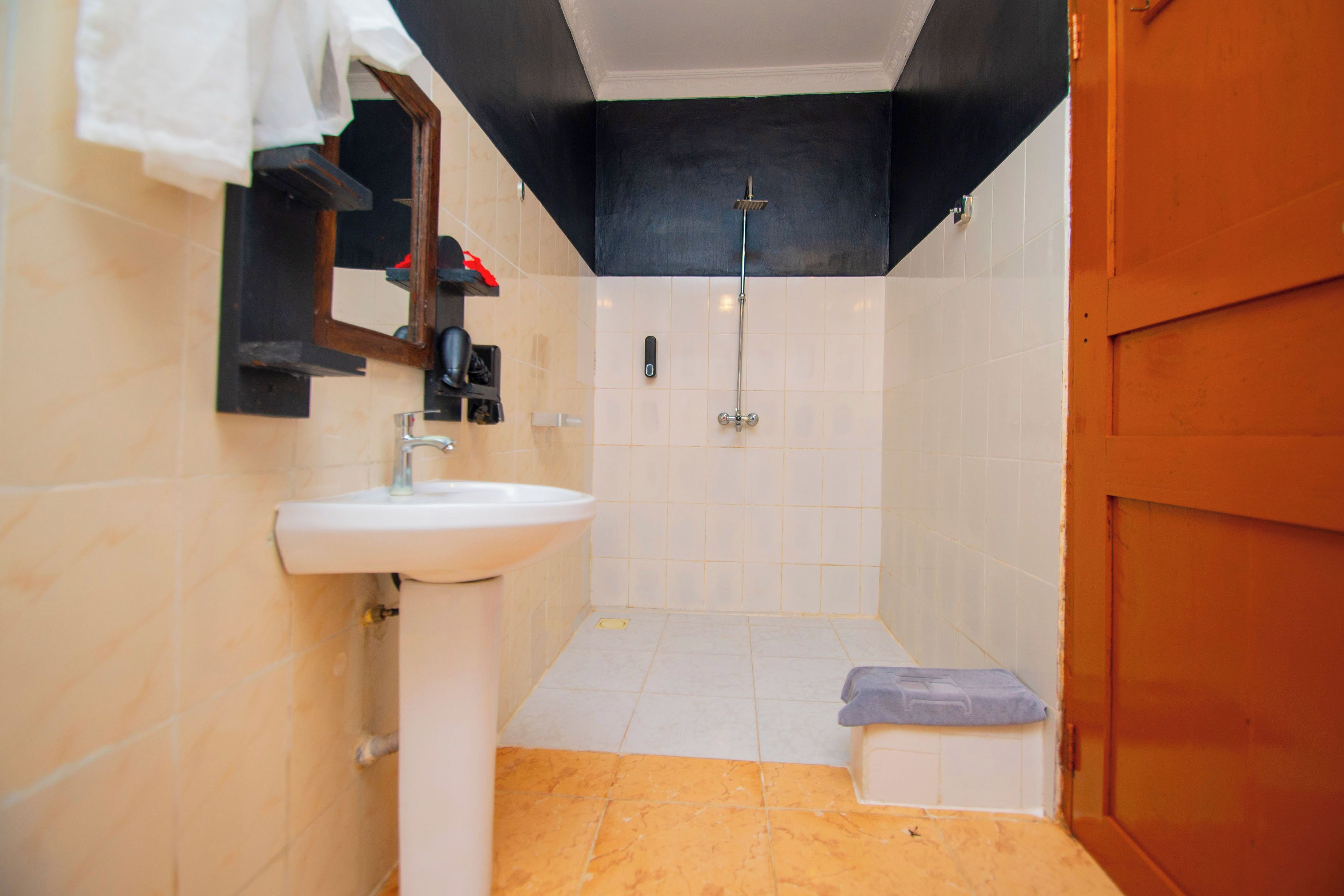 Un baño con lavamanos blanco, ducha y puerta de madera.