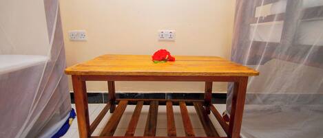A wooden table with a red flower on it, positioned in a room with a plain wall and a power outlet.