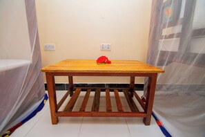 Una mesa de madera con una flor roja, ubicada en una habitación con una pared lisa y un enchufe.