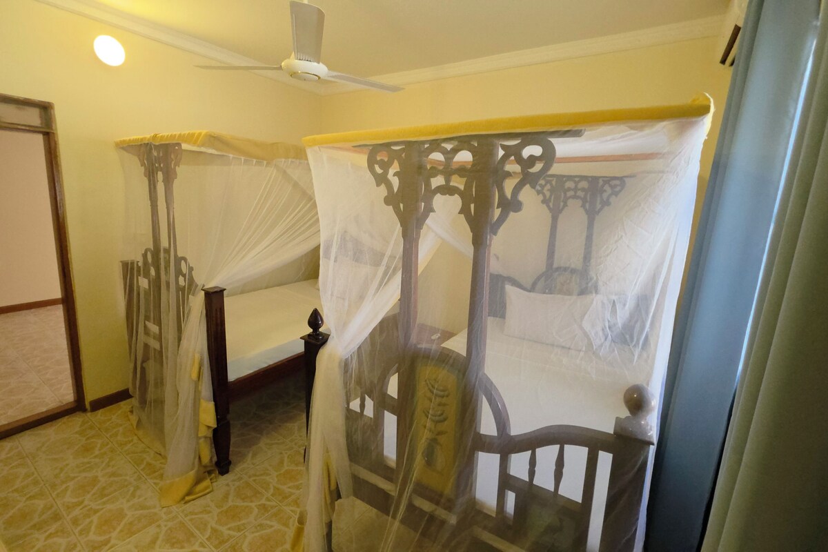 Una habitación con dos camas individuales, un ventilador de techo y una mosquitera.
