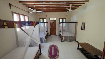 Una stanza con due letti, una panca, una porta e una ventola a soffitto.