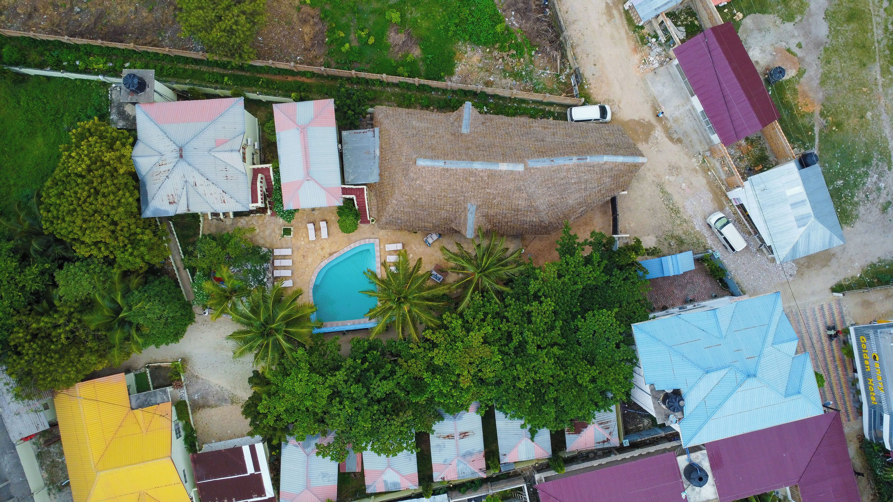 An aerial view of a residential area with a swimming pool, multiple houses, and a fenced garden area.