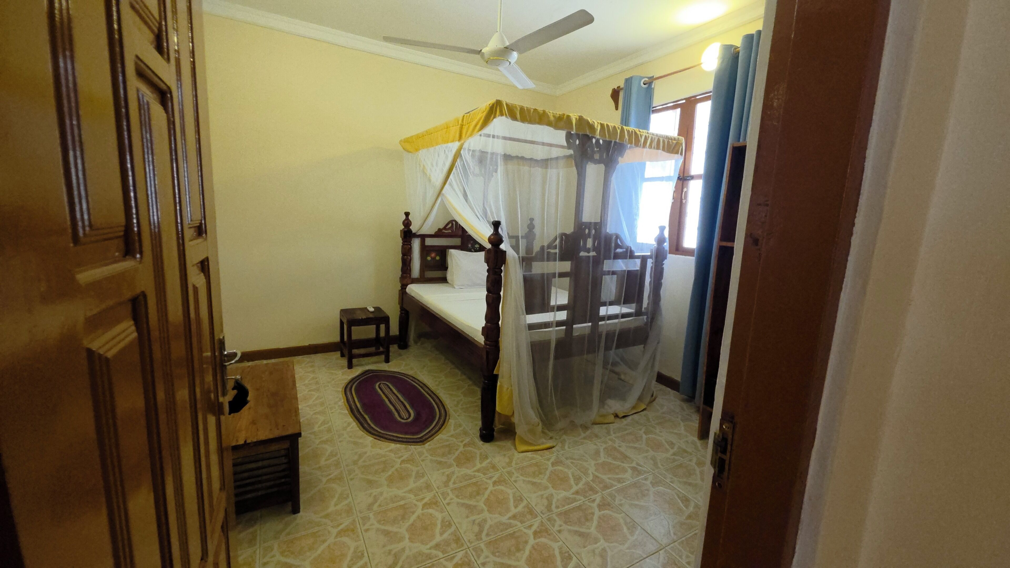 A room with a bed, a ceiling fan, a small table, and a patterned rug.