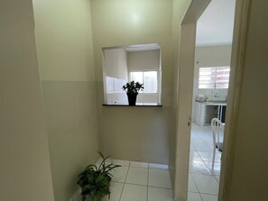 Un pasillo estrecho con una planta en maceta, un espejo en la pared y una vista parcial de una cocina.