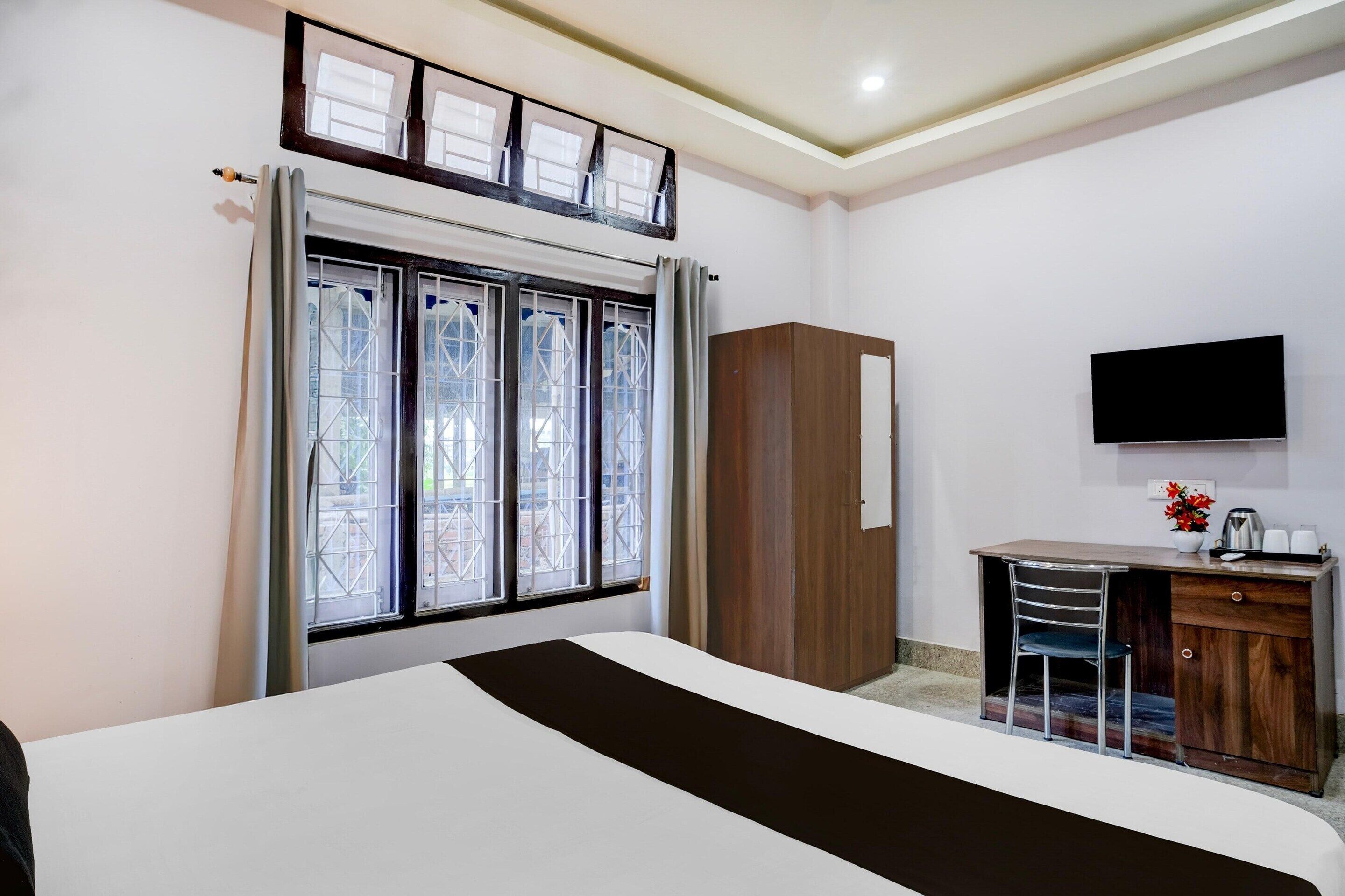 A hotel room with a bed, a desk with a chair, a wardrobe, a television, and a window with curtains.