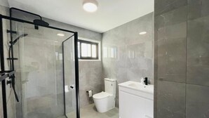 A modern bathroom with a glass shower enclosure, a toilet, and a white vanity. - 262Troughton (Coopers Plains)
