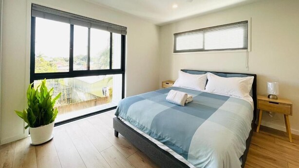 A bedroom with a bed, a ceiling fan, a window, a nightstand, and a potted plant. - 262Troughton (Coopers Plains)