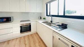 A modern kitchen with white cabinetry, a built-in oven, a microwave, a sink, and a window with blinds. - 262Troughton (Coopers Plains)