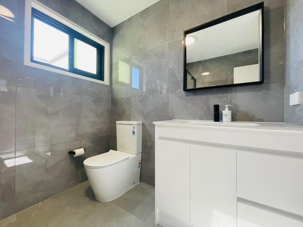 Een badkamer met toilet, wastafel, spiegel en raam.