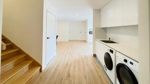A modern kitchen with built-in appliances, a wooden staircase, and a hallway leading to another room. - 262Troughton (Coopers Plains)