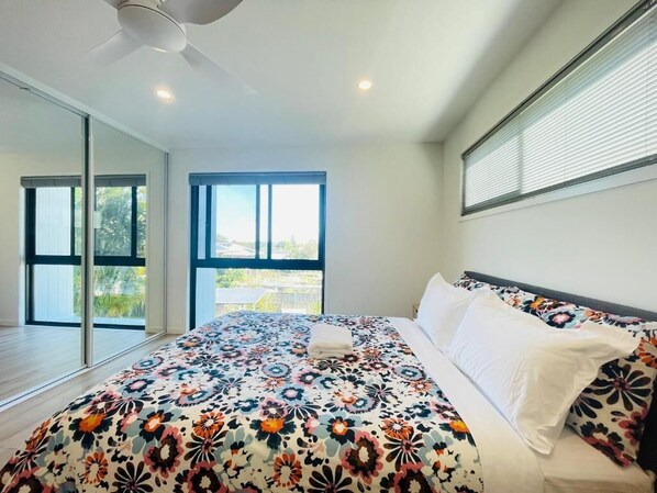 A bedroom with a large bed, a ceiling fan, and a view through a sliding glass door. - 262Troughton (Coopers Plains)