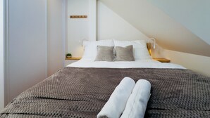 A modern bedroom with a bed, pillows, a bedside table, a lamp, and a wall-mounted shelf.