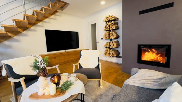 A modern living room with a staircase, a fireplace, a flat-screen TV, and a dining area with candles and a decorative centerpiece.