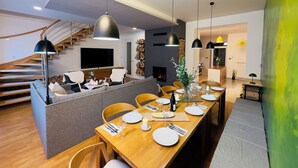A modern living room with a dining area, wooden staircase, and a fireplace.
