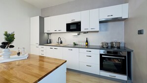 A modern kitchen with white cabinetry, a wooden countertop, a built-in oven, and a microwave.