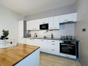 A modern kitchen with white cabinetry, a wooden countertop, a built-in oven, and a microwave. - Mountain Retreat in Jáchymov (Jáchymov)
