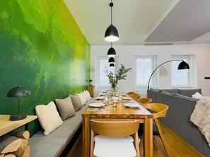 A dining area with a wooden table set for four, a sofa, and a green accent wall. - Mountain Retreat in Jáchymov (Jáchymov)