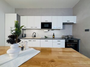 A modern kitchen with white cabinets, a microwave, and a wooden countertop. - Mountain Retreat in Jáchymov (Jáchymov)