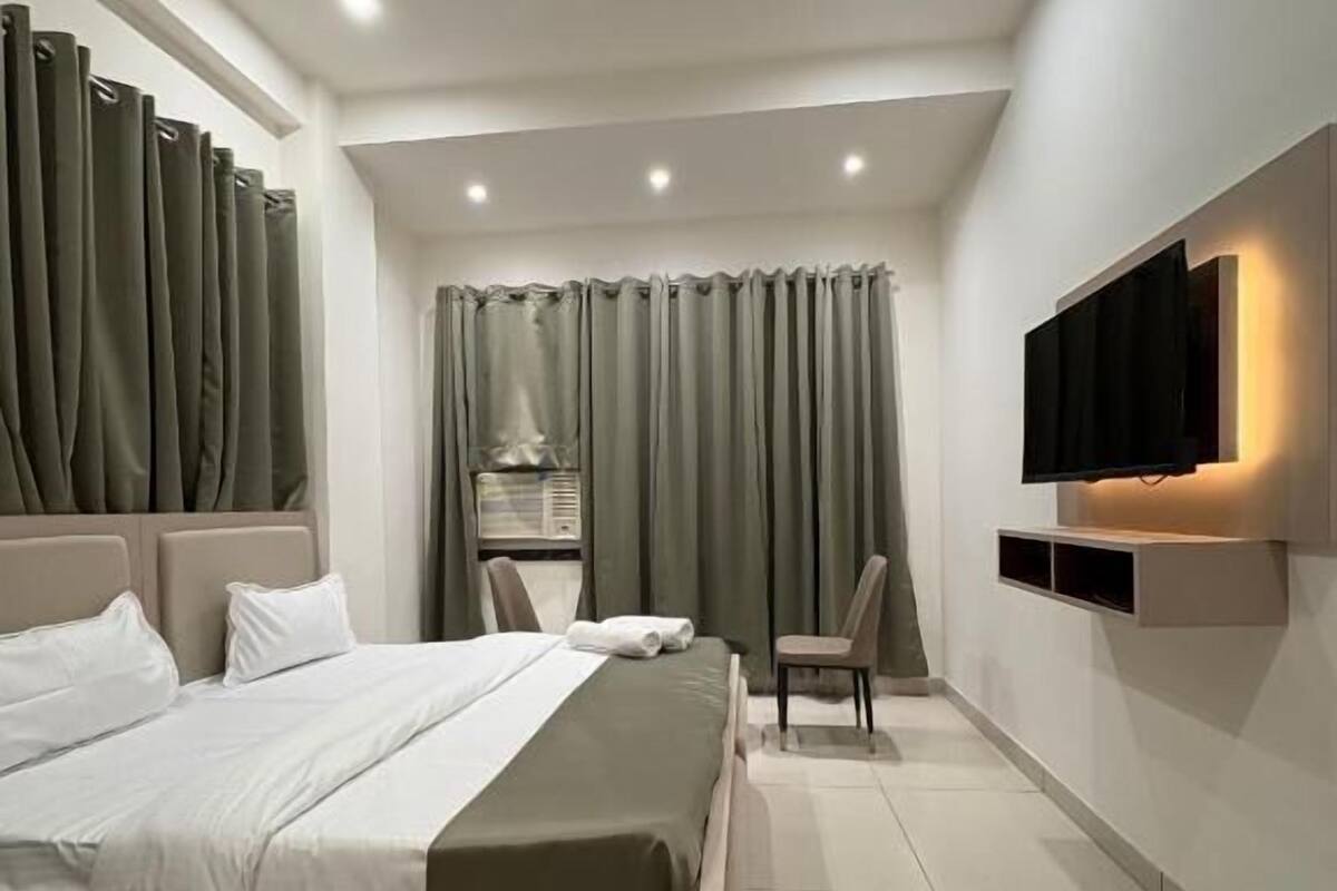 A modern hotel room with a large bed, a ceiling fan, a TV mounted on the wall, and a small seating area.