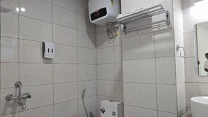 A bathroom with a toilet, a sink, a towel rack, and a shower. - Shft-In Hotel (Noida)