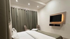 A modern bedroom with a bed, curtains, a TV, and a ceiling fan. - Shft-In Hotel (Noida)