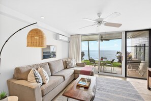 Ein modernes Wohnzimmer mit Sofa, Couchtisch und Meerblick durch große Glasfenster.