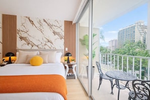 Een hotelkamer met een groot bed, een balkon met een tafel en stoelen en uitzicht over de stad.