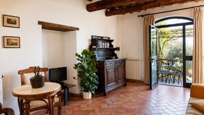 A room with a wooden ceiling, a dining table with chairs, a television, a cabinet with books, a potted plant, and a view through a glass door. - Romantic Tuscan Retreat With Pool (Castelnuovo Berardenga)