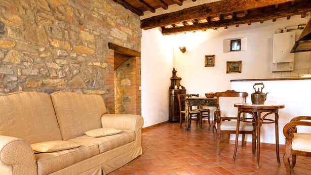 A cozy living area with a stone wall, a sofa, wooden dining table, chairs, and a tiled floor. - Romantic Tuscan Retreat With Pool (Castelnuovo Berardenga)