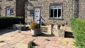 Un bâtiment en pierre avec une porte blanche, des fenêtres numérotées et des plantes en pot.