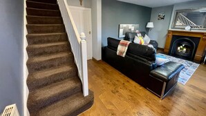 Un escalier avec des marches recouvertes de moquette et des balustrades blanches, un canapé en cuir noir avec un plaid, une cheminée et un plancher en bois.