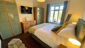 Une chambre à coucher avec un lit, une télévision, une commode et une fenêtre avec des rideaux.