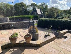 A stone patio with potted plants, a stone wall, and a hedge.
