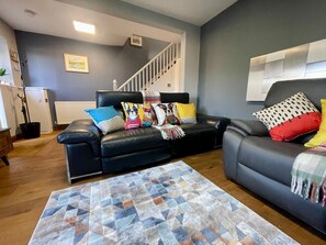 A living room with a black leather sofa, a patterned rug, and a staircase in the background.